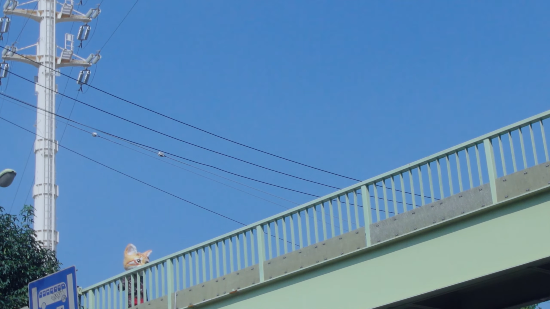 A girl wearing an orange cat head walking across a bridge.